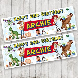 May include: Two banners with the text "HAPPY 2ND BIRTHDAY ARCHIE" and cartoon characters from the Toy Story film. The banners feature Woody, Buzz Lightyear, Jessie, and other characters.