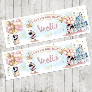 May include: Two banners with a light blue background, featuring Minnie Mouse illustrations, balloons, and a castle. The text reads "Happy 1st Birthday Amelia". Gold confetti dots the background.