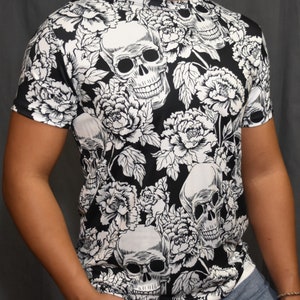 Pode incluir: Camiseta preta e branca com um padrão de caveira e flores. As caveiras são contornadas em branco e as flores são brancas com centros pretos.