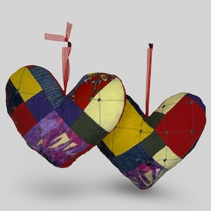 May include: Two heart-shaped fabric decorations with patchwork patterns in red, yellow, purple, and blue. Each heart has a red ribbon for hanging. These hearts are a charming decorative item.