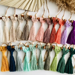 May include: A collection of 20 handmade cinnamon stick ornaments with colorful macrame tassels. The ornaments are tied with twine and have wooden beads.