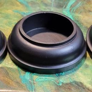 May include: Four black round bowls of varying sizes, with a smooth, glossy finish. The bowls are arranged in a row from smallest to largest, on a green and blue surface.