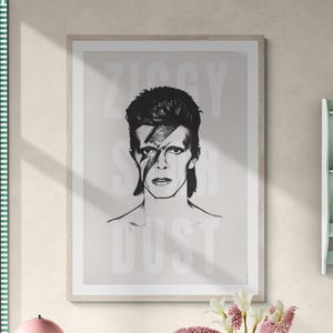 Może przedstawiać: Oprawiony czarno-biały portret Davida Bowiego z napisem "Ziggy Stardust" w tle. Portret przedstawia Bowiego z błyskawicą na twarzy. Obraz jest wyświetlany w jadalni.
