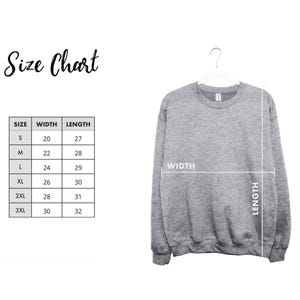 a gray sweatshirt hanging on a hanger, with a size chart and measurements displayed next to it.