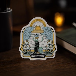 May include: A die-cut sticker featuring a graphic illustration of a person in a hat and long dress standing with a suitcase. The scene includes a sun, clouds, and flowers, framed in an archway with the text FOREVER WANDER at the bottom.