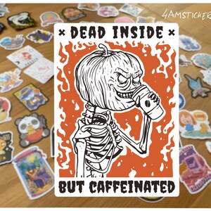 Może przedstawiać: Biała naklejka z szkieletem z dyniową głową pijącym kawę, otoczonym pomarańczowymi płomieniami. Tekst brzmi „DEAD INSIDE BUT CAFFEINATED”. Tło przedstawia różne kolorowe naklejki.