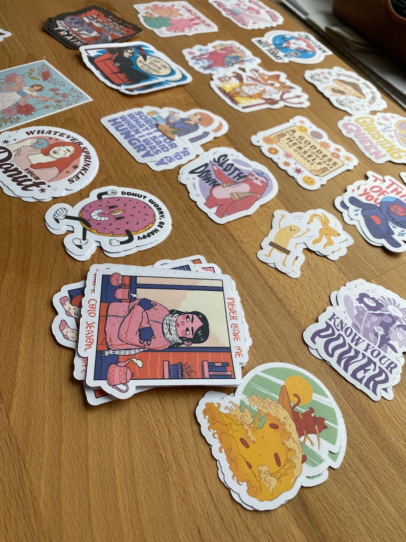 May include: A collection of colorful stickers featuring various illustrations and text. Some of the stickers include a donut with the text "Donut worry, be happy", a woman with the text "Whatever sprinkles", a sloth with the text "Sloth", and a person with the text "Cold Season".
