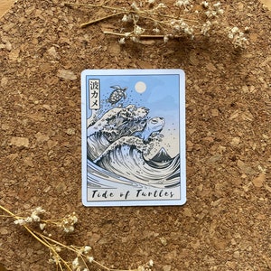 May include: A blue and white tarot card with a wave and four sea turtles. The card is titled "Tide of Turtles" and has Japanese text in the top left corner.