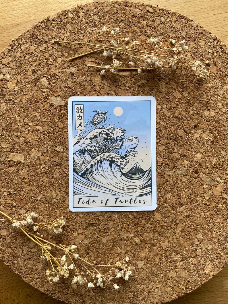 May include: A blue and white tarot card with a wave and four sea turtles. The card is titled "Tide of Turtles" and has Japanese text in the top left corner.