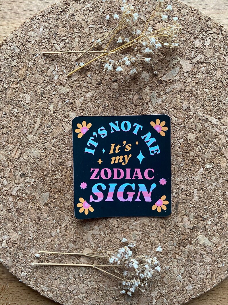 May include: Black sticker with white, pink, and blue text that reads "It's not me, It's my Zodiac Sign" with flower accents.