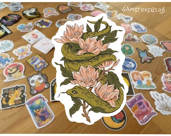Pode incluir: Um autocolante com uma cobra verde enrolada em flores cor de pêssego e folhas verdes. O autocolante tem o texto "4AMSTICKERCLUB". O fundo é uma superfície de madeira salpicada com vários autocolantes.