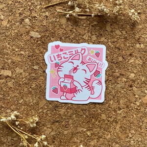 Pode incluir: Um adesivo rosa e branco com um gato de desenho animado bebendo leite de morango. O gato est&aacute; usando uma coleira rosa e tem uma express&atilde;o feliz. O adesivo diz "いちごミルク" em japon&ecirc;s, o que significa "leite de morango", e "おいしい!" que significa "delicioso!"