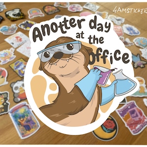 Può includere: Un adesivo con una lontra dei cartoni animati con occhiali protettivi e guanti blu, che tiene in mano beute con liquidi. Il testo "Another day at the office" è sopra la lontra. Lo sfondo è una superficie di legno con vari adesivi.