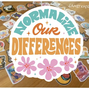 Könnte beinhalten: Eine Sammlung von Aufklebern auf einer Holzoberfläche. Der zentrale Aufkleber trägt den Text "Normalize Our Differences" in Türkis und Orange, mit rosa Blumenakzenten. Andere Aufkleber zeigen verschiedene Designs und Farben.