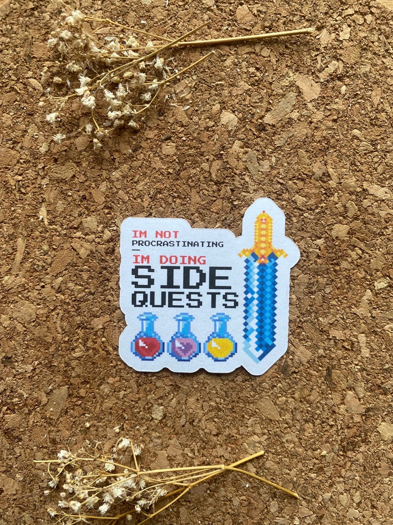May include: A white sticker with a blue pixelated sword and three pixelated potion bottles. The text on the sticker reads "I'm not procrastinating I'm doing side quests."