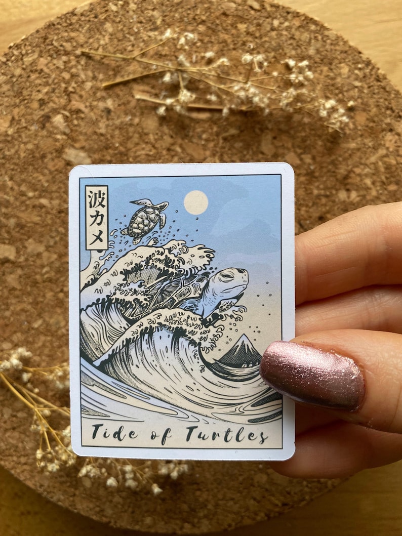 May include: A sticker with a Japanese-inspired design featuring a large wave with three turtles on top. The text "Tide of Turtles" is printed below the wave. The Japanese text "波カメ" is printed in the top left corner.