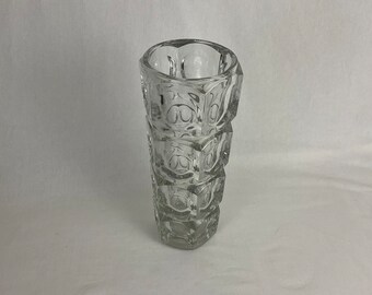 Op de afbeelding: Een heldere glazen vaas met een geometrisch ontwerp. De vaas is gemaakt van dik glas en heeft een zeshoekige vorm.
