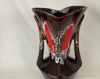 May include: A brown ceramic vase with a unique shape and design. The vase features a dark brown base and sides, with a red and white pattern in the center. It has two handles and a flared top.