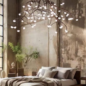 以下が含まれることがあります： ベージュの毛布と枕が置かれた木製のプラットフォームベッド。ベッドは、多くの光がついた木の枝のようなユニークな大きなシャンデリアのある部屋にあります。