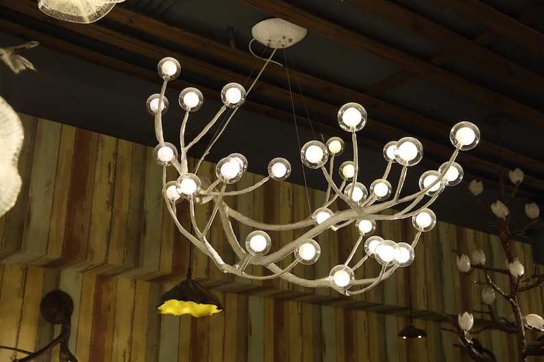 May include: A white, branch-like chandelier with multiple clear glass bulbs. The chandelier is hanging from a ceiling with wooden beams.