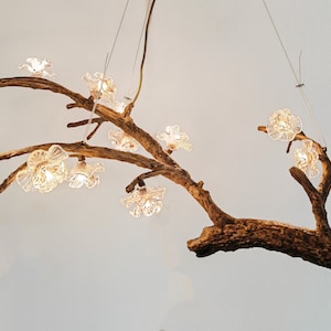 May include: A rustic wooden branch chandelier with clear glass flower-shaped lights and a bird figurine. The chandelier is hanging from the ceiling.