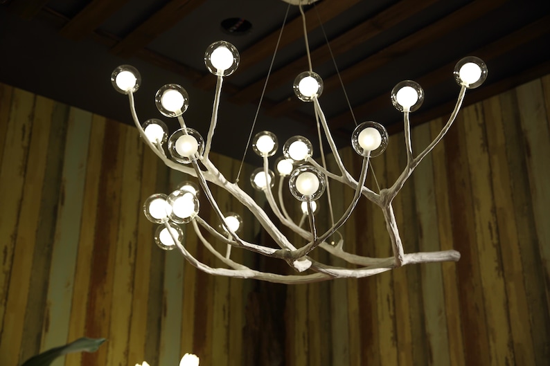 May include: A white metal chandelier with a tree branch design and multiple round glass bulbs. The chandelier is hanging from a ceiling with wooden beams.