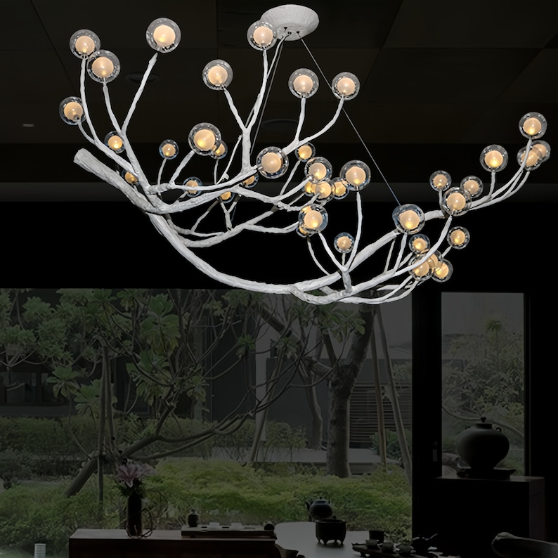 May include: A white metal chandelier with a tree branch design and multiple clear glass globes with warm white lights.