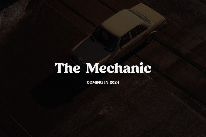 May include: A high-angle view of a tan sedan parked on a dark surface. The text "The Mechanic" appears in white serif font in the center, with the text "COMING IN 2024" positioned directly below it in a smaller, bold white sans-serif typeface.