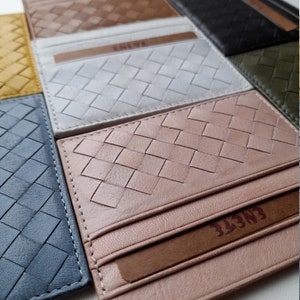 Puede incluir: Una colecci&oacute;n de tarjeteros de cuero tejido en varios colores, incluyendo marr&oacute;n, blanco, rosa y azul. Cada tarjetero presenta un patr&oacute;n texturizado de tejido de cesta y una ranura para tarjetas. La marca "ENETE" es visible.