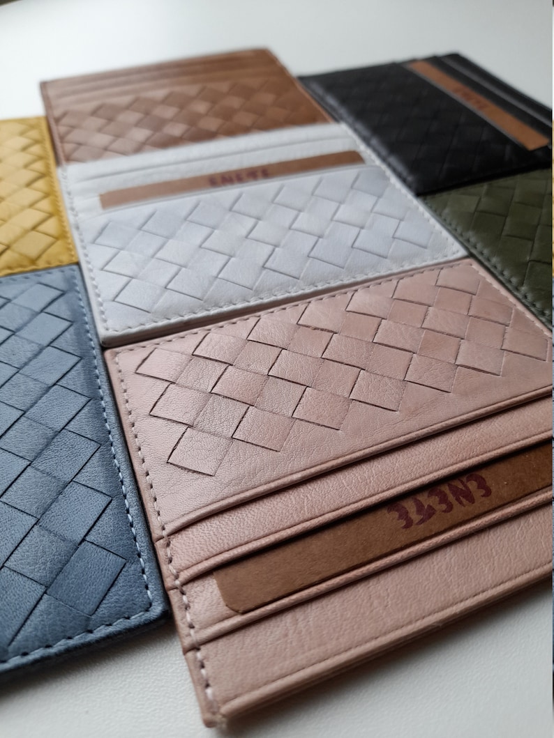 Puede incluir: Una colecci&oacute;n de tarjeteros de cuero tejido en varios colores, incluyendo marr&oacute;n, blanco, rosa y azul. Cada tarjetero presenta un patr&oacute;n texturizado de tejido de cesta y una ranura para tarjetas. La marca "ENETE" es visible.