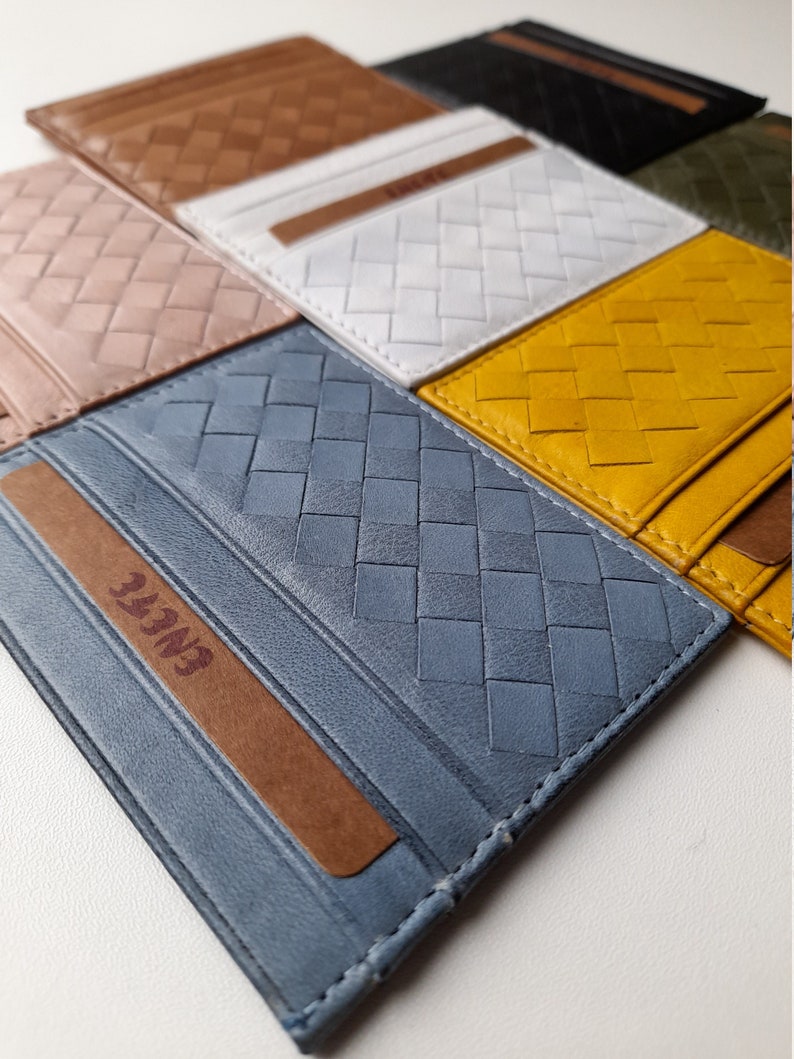 Puede incluir: Una colecci&oacute;n de tarjeteros de cuero trenzado en varios colores, incluyendo marr&oacute;n, blanco, amarillo y azul. Cada tarjetero tiene un dise&ntilde;o rectangular con un patr&oacute;n trenzado y una tira de acento marr&oacute;n. La palabra "ENLIFE" es visible.