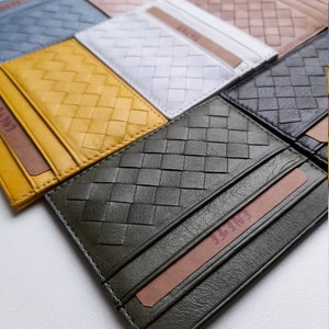 Puede incluir: Una colecci&oacute;n de tarjeteros de cuero tejido en varios colores, incluyendo amarillo, azul, blanco y verde oliva. Cada tarjetero presenta un dise&ntilde;o tejido y una ranura para tarjetas. El nombre de la marca es visible en una tarjeta dentro.