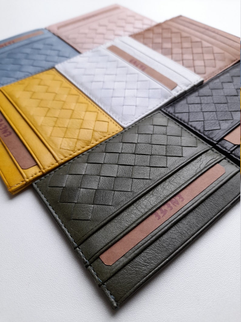 Puede incluir: Una colecci&oacute;n de tarjeteros de cuero tejido en varios colores, incluyendo amarillo, azul, blanco y verde oliva. Cada tarjetero presenta un dise&ntilde;o tejido y una ranura para tarjetas. El nombre de la marca es visible en una tarjeta dentro.