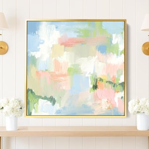 Puede incluir: Una pintura abstracta con marco dorado cuelga sobre una consola de madera clara. La obra presenta colores pastel, incluyendo rosa, azul y verde. Dos jarrones blancos con flores se encuentran sobre la mesa, y dos apliques dorados flanquean la obra.