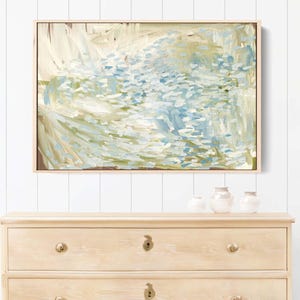 May include: A light wood dresser with three drawers, brass hardware, and a framed abstract painting above it. Two green rain boots stand beside the dresser. A potted plant sits to the right.