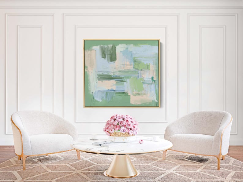 May include: A living room interior with two cream armchairs, a marble coffee table, and an abstract painting with green, blue, and beige tones. A pink floral display is on the table. The room has a neutral colour palette.