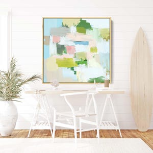 May include: Abstract art painting in a gold frame. The artwork features brushstrokes of blue, green, pink, and beige. The painting hangs above a white desk with a white chair. A surfboard leans against the wall.