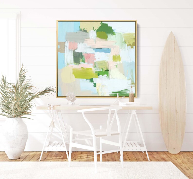 May include: Abstract art painting in a gold frame. The artwork features brushstrokes of blue, green, pink, and beige. The painting hangs above a white desk with a white chair. A surfboard leans against the wall.