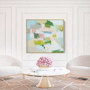 May include: An abstract painting in a gold frame hangs above a marble-topped coffee table and two white armchairs. The painting features pastel colours, including pink, green, and blue. A bouquet of pink flowers sits on the table.