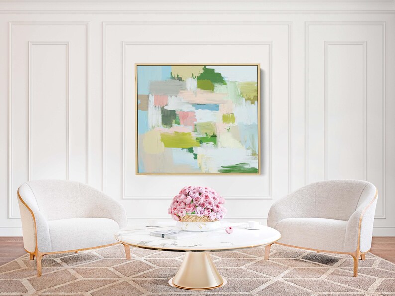 May include: An abstract painting in a gold frame hangs above a marble-topped coffee table and two white armchairs. The painting features pastel colours, including pink, green, and blue. A bouquet of pink flowers sits on the table.