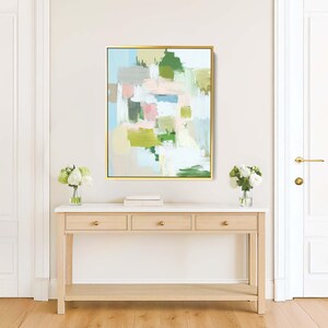 May include: Abstract art painting in a gold frame. The artwork features a mix of pastel colours, including green, pink, and blue, arranged in a blocky, brushstroke style. The painting hangs above a light wood console table.