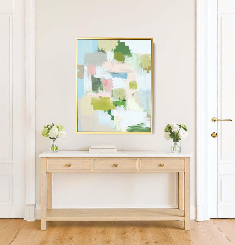 May include: Abstract art painting in a gold frame. The artwork features a mix of pastel colours, including green, pink, and blue, arranged in a blocky, brushstroke style. The painting hangs above a light wood console table.