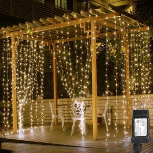 May include: A set of warm white LED fairy lights strung across a wooden pergola. The lights are arranged in a curtain-like pattern, creating a warm and inviting ambiance. The lights are plugged into an electrical outlet.