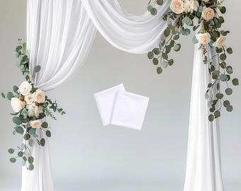 Może przedstawiać: Białe, przezroczyste zasłony z tkaniny są zawieszone na drewnianym belce, tworząc tło dla ceremonii ślubnej lub wydarzenia. Tkanina jest zebrana i udrapowana w płynnym, eleganckim stylu. Po prawej stronie obrazu znajdują się zielone liście i białe kwiaty, dodając scenie odrobinę naturalnego piękna.