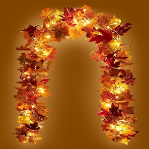 Peut inclure: Une guirlande en arc composée de feuilles d'automne artificielles dans des tons de rouge, orange, jaune et marron. Le feuillage est entremêlé de petites guirlandes lumineuses LED blanc chaud qui diffusent une lueur douce sur les feuilles.