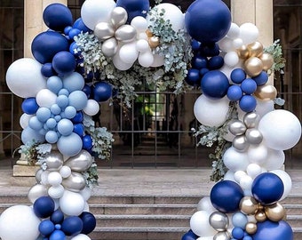 May include: A balloon arch made of blue, white, and gold balloons. The arch is decorated with greenery and is perfect for a wedding, birthday, or other special event.
