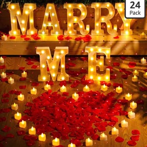 May include: Lit-up letters spelling "MARRY ME" with small candles and red rose petals arranged in a heart shape. The letters are illuminated with warm white lights, creating a romantic ambiance. The scene is set on a wooden surface.