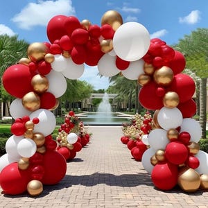 May include: A red, white, and gold balloon archway for a wedding or party. The archway is made of balloons of different sizes and is decorated with red, white, and gold balloons.
