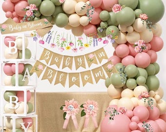 May include: A baby shower decoration set featuring a balloon arch in pink, green, and cream colors, with floral accents. The set includes a banner that reads "Baby in Bloom" and decorative boxes with balloons and letters spelling "BABY".