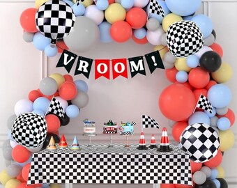May include: A checkered black and white tablecloth with a checkered black and white balloon arch and a banner that says "VROOM!" in red and black letters. There are also red, yellow, blue, and gray balloons in the arch. There are small checkered black and white balloons, and red and white checkered flags.